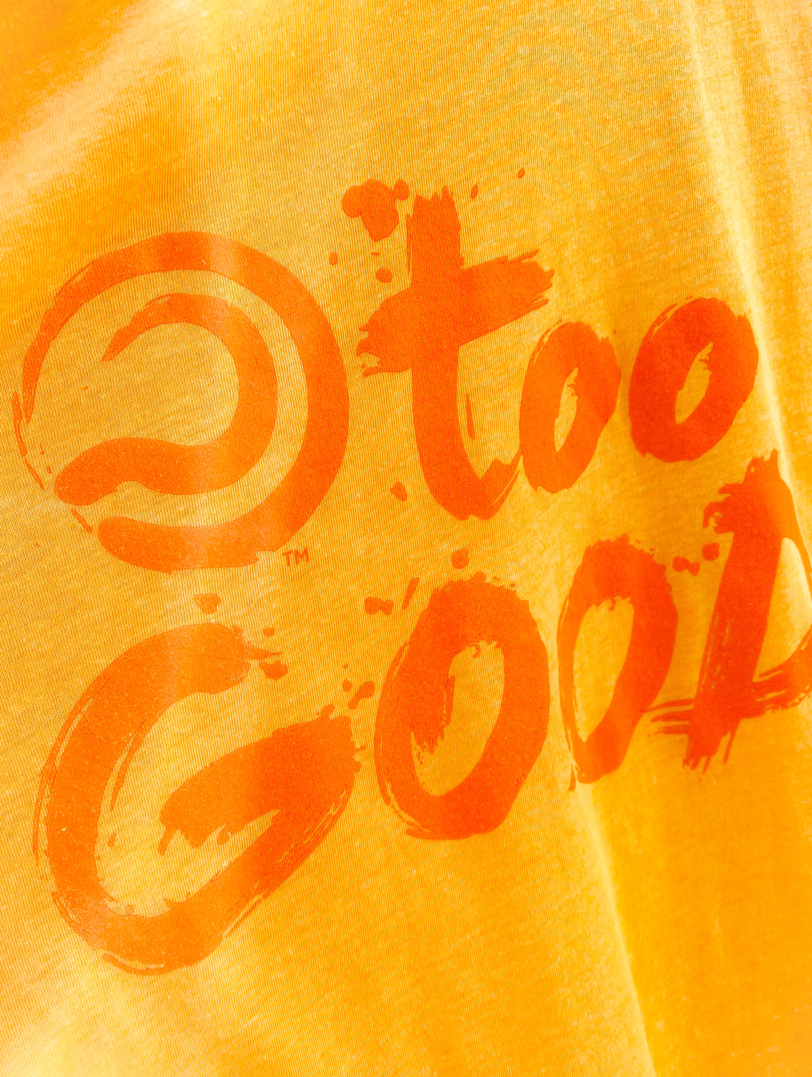 Extreme close up shot of a Too Good graphic on a bright yellow shirt.