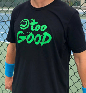 Shot of a tennis player's torso while wearing Black shortsleeve t-shirt with green Too Good graphic in front of a fence at a tennis court. Wearing blue wrist bands.