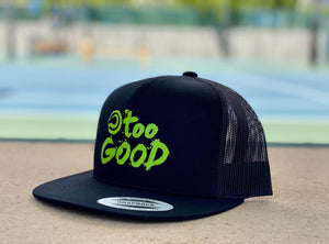 Too Good black trucker hat with mesh back and a snapback with a lime green Too Good graphic sitting on a bench in front of a blurred out blue tennis court background during the middle of the day.