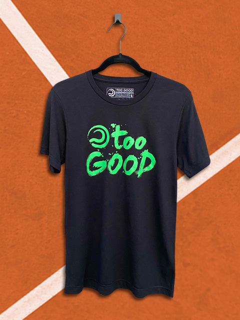 Black Too Good tennis t-shirt with a green graphic that says too good with a ball mark, hanging from a black hanger in front of an orange tennis court background.